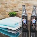 Two bottles of 'Men's Blend Care' beard products on a reflective surface with folded towels and a plant in the background.