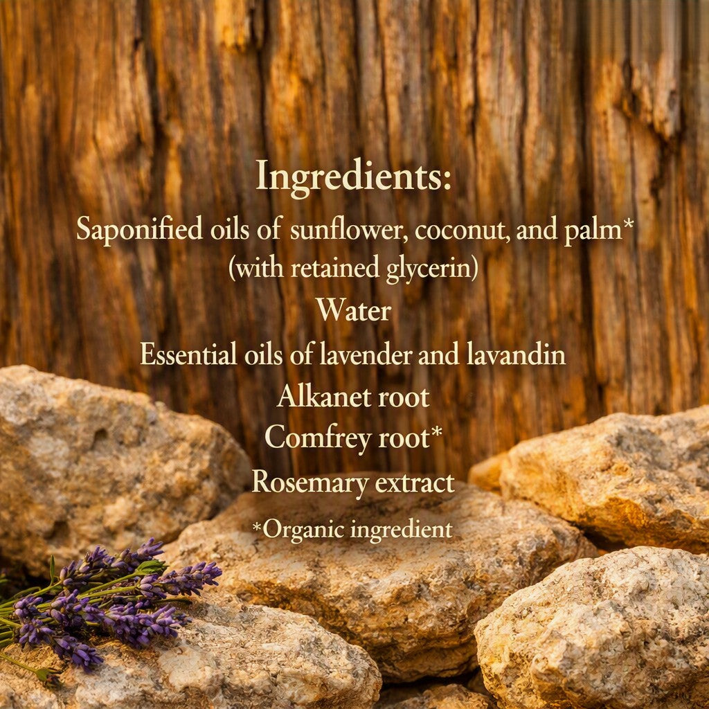 Ingredients list text over a rustic wood and stone background with lavender sprigs. The text reads: Ingredients: Saponified oils of sunflower, coconut, and palm* (with retained glycerin), Water, Essential oils of lavender and lavandin, Alkanet root, Comfrey root*, Rosemary extract, and *Organic ingredient*.